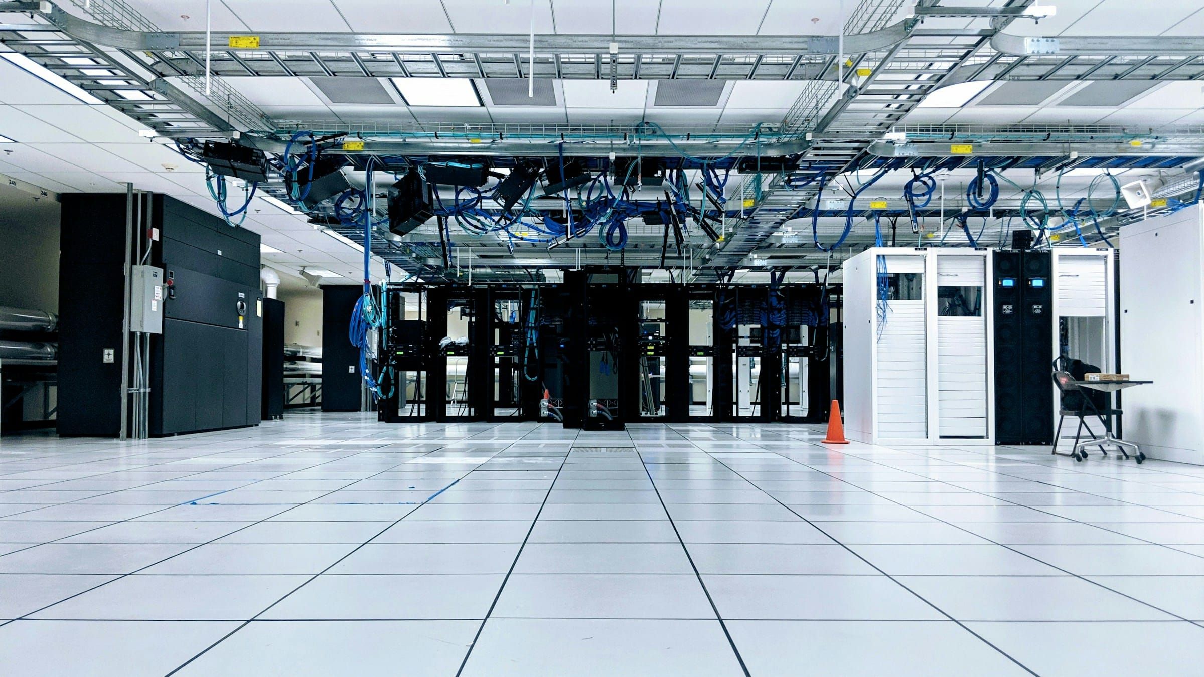 Bright, white raised-floor data center with rows of server racks and blue network cables running through overhead trays