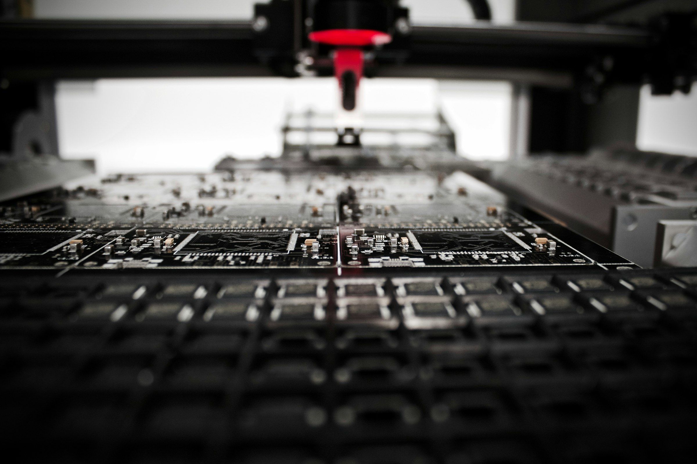 Pick-and-place machine head above black circuit boards on an electronics assembly line