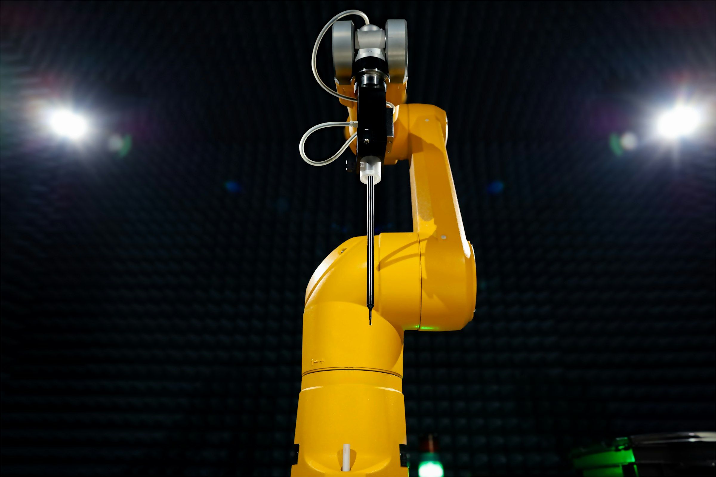 Close-up of a yellow six-axis robot arm with a probe tool, spotlit in a dark test chamber