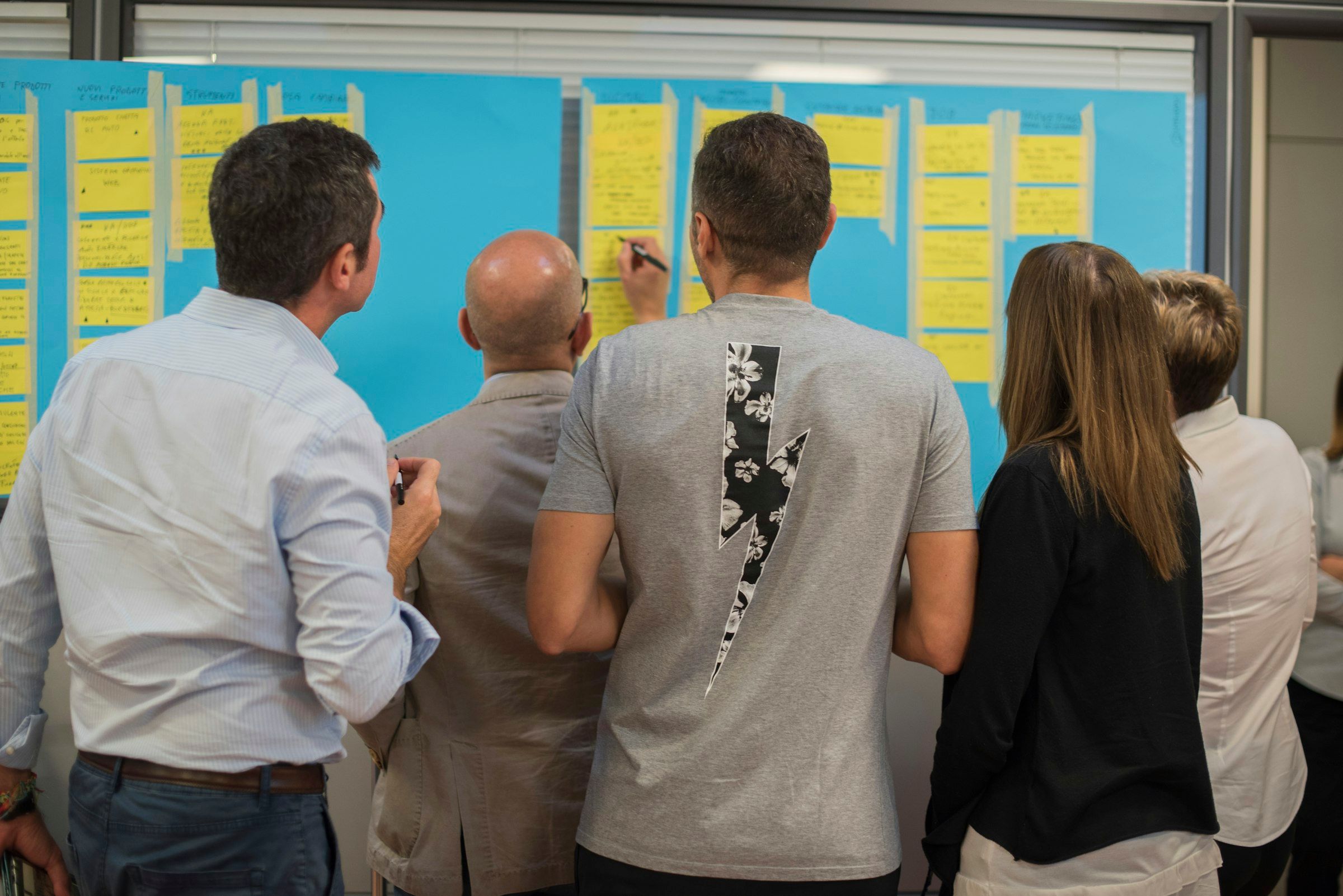 Small team at a workshop wall, writing on columns of yellow sticky notes