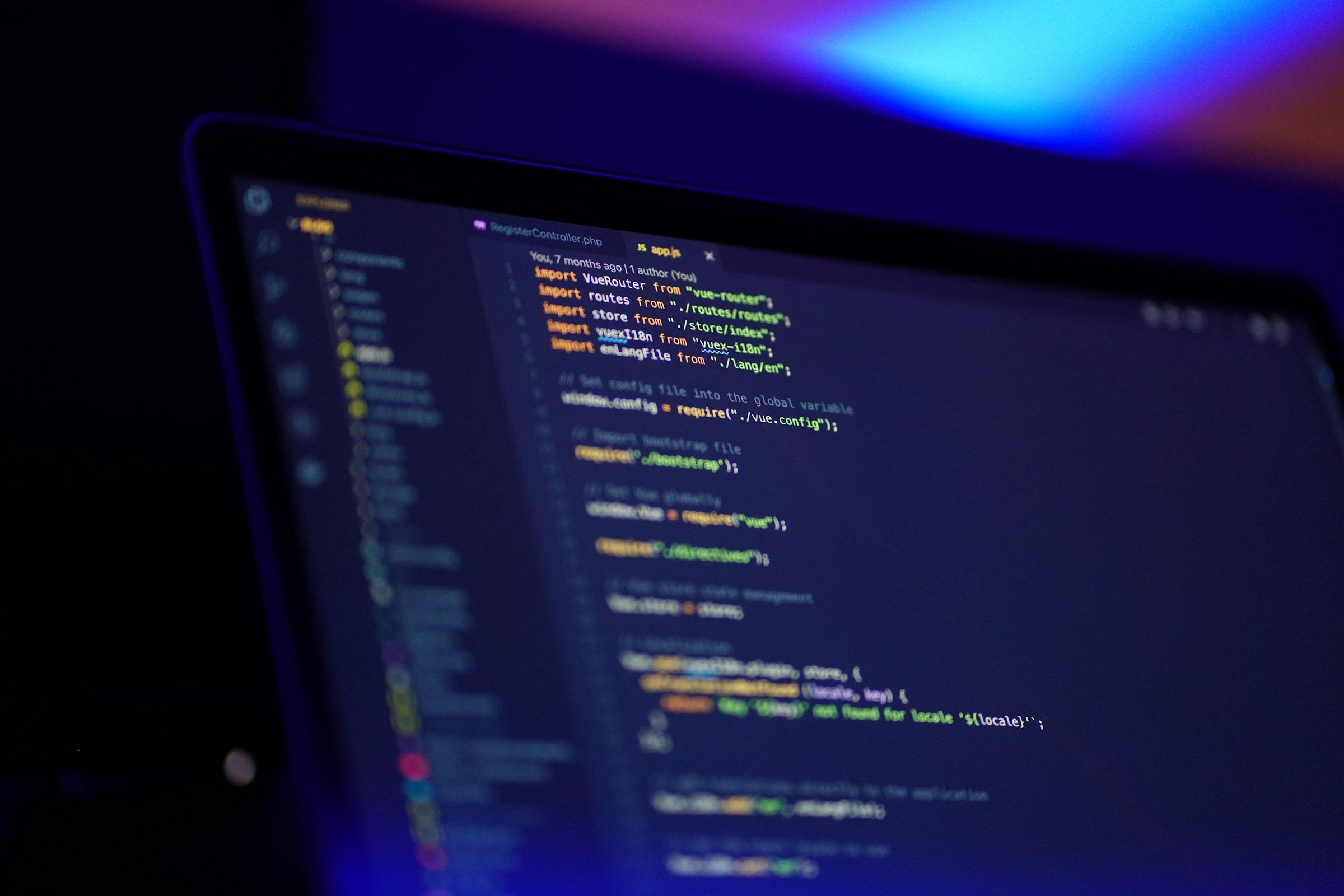 Laptop screen showing syntax-highlighted source code in an editor, lit by blue and purple light